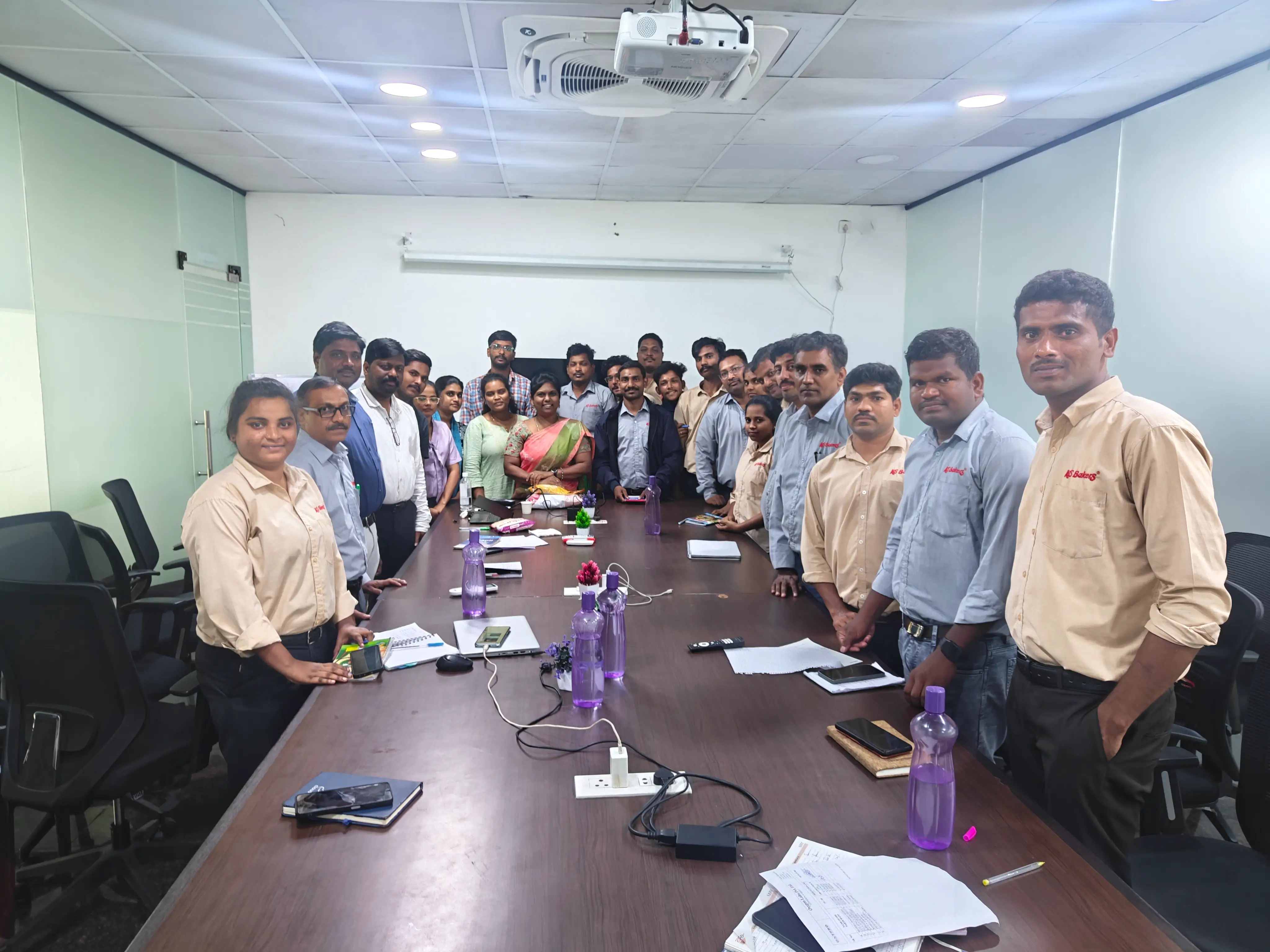 Participants standing around a long boardroom table at the close of an in-house training session.