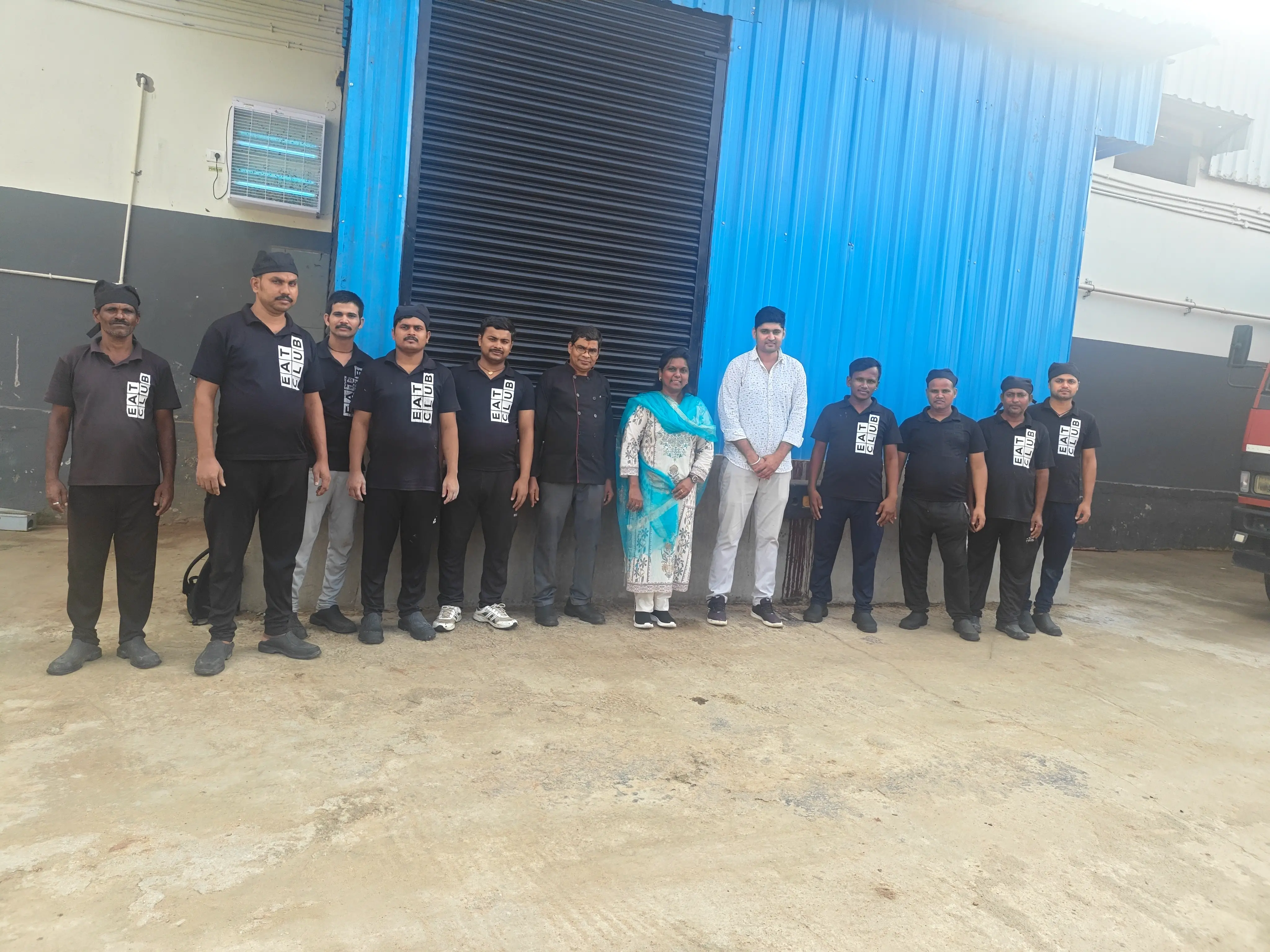 Factory team in uniform lined up for a group photograph in front of an industrial shed.