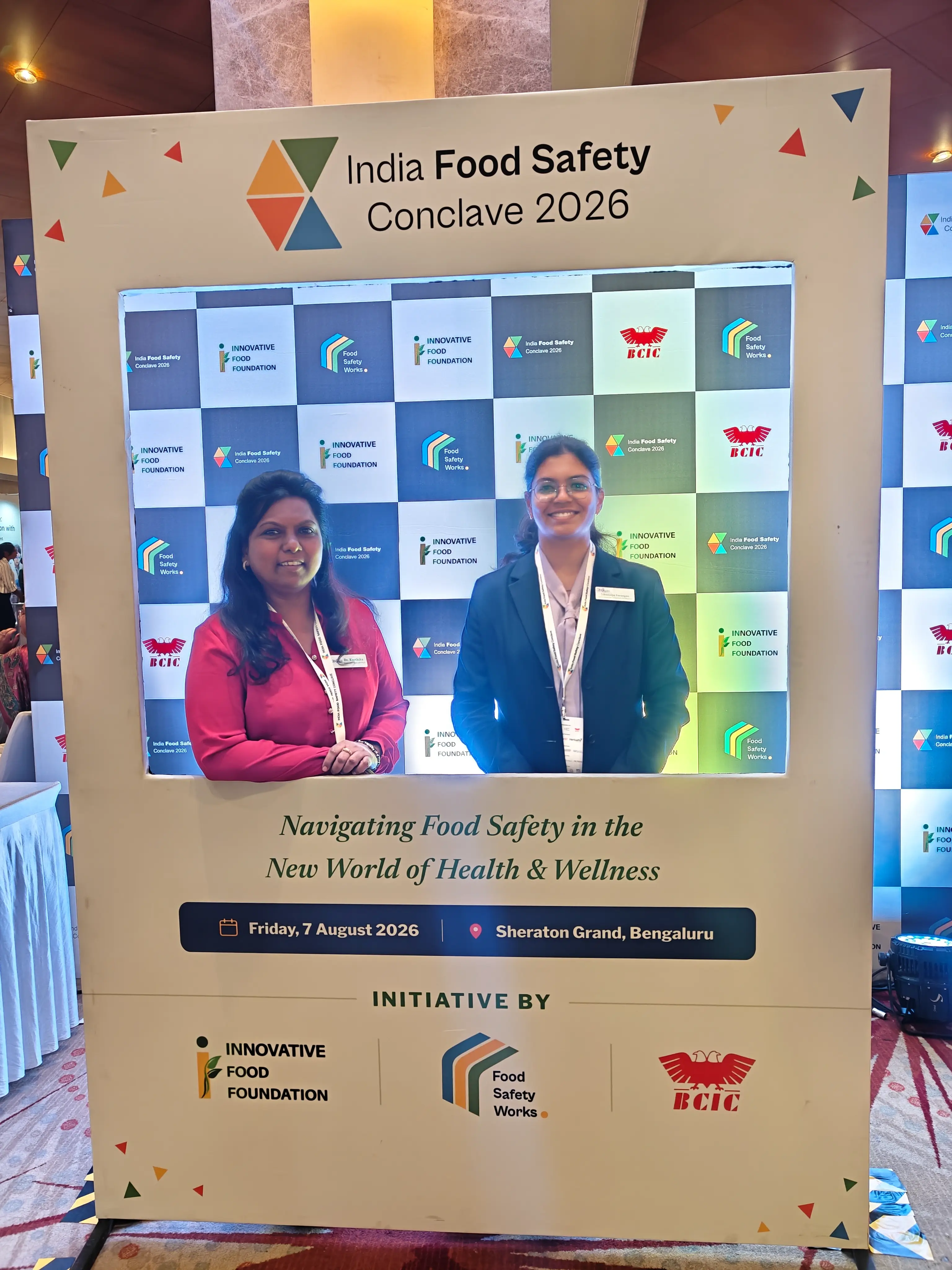 Two delegates standing inside a photo frame branded for the India Food Safety Conclave 2026.