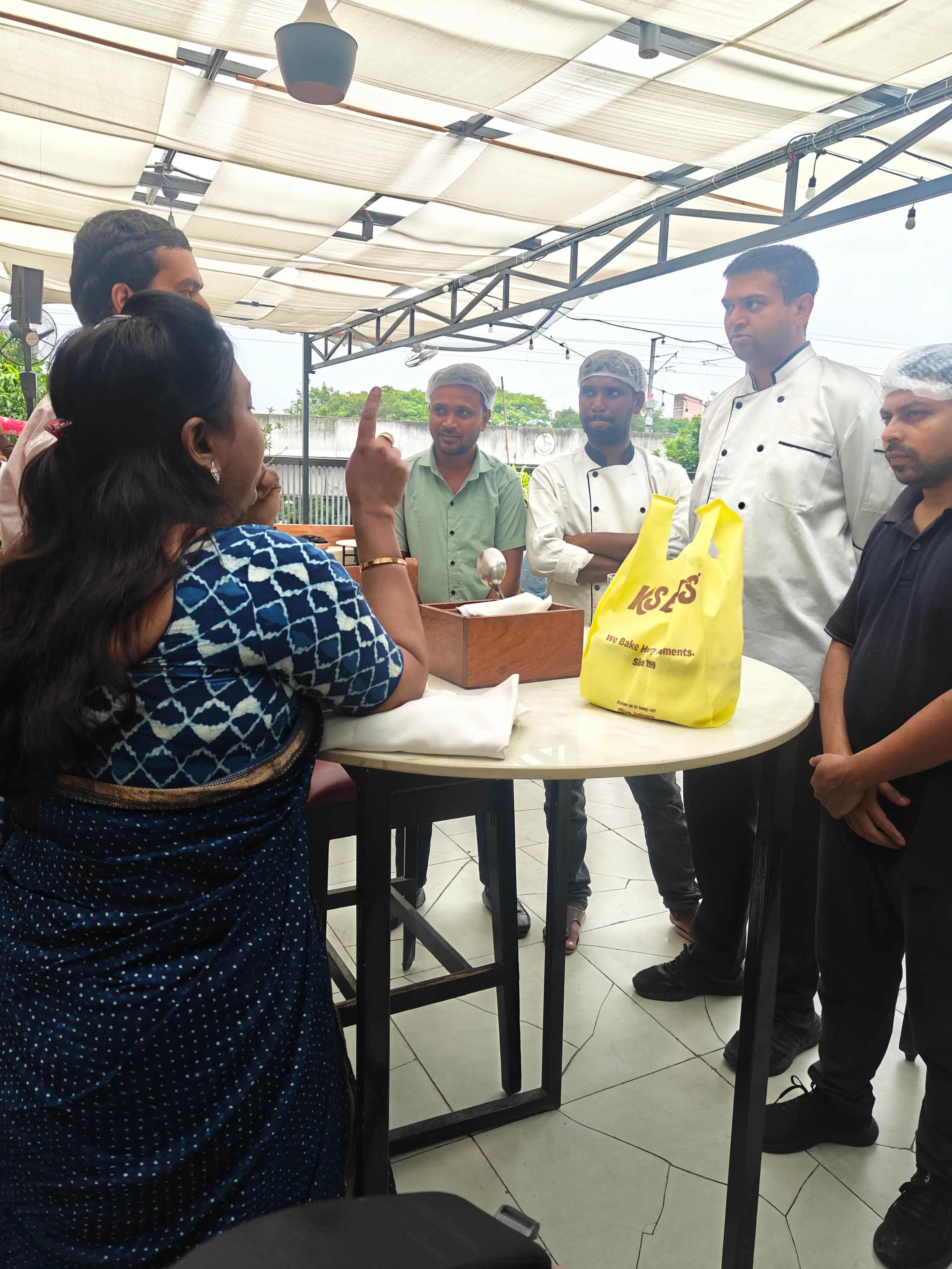 Staff gathered around a table in an outdoor seating area examining packed food items during an on-site review.