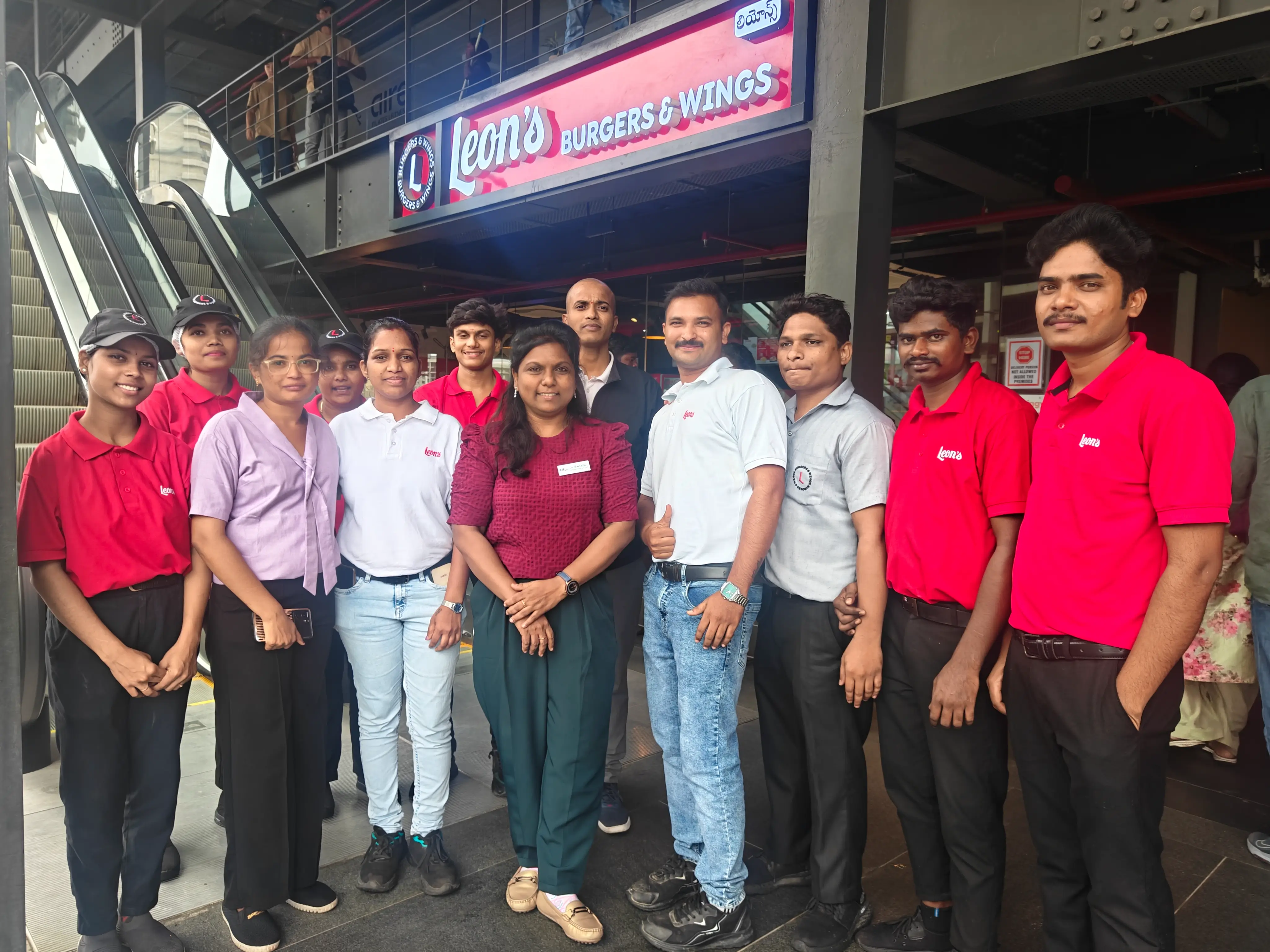 Restaurant outlet staff in uniform standing together with visiting professionals in front of the service counter.
