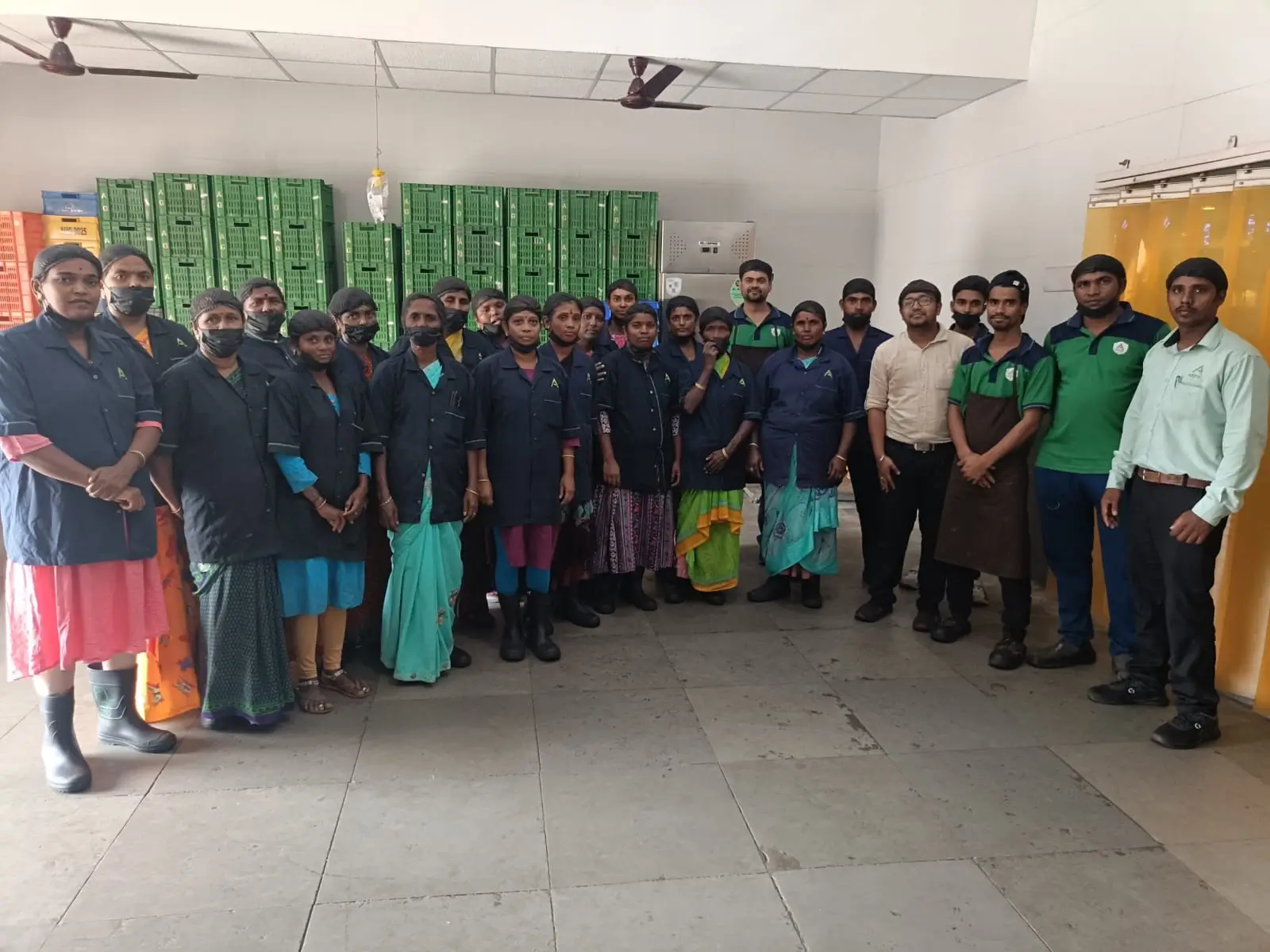 Large warehouse team standing together for a group photograph in front of stacked green crates.